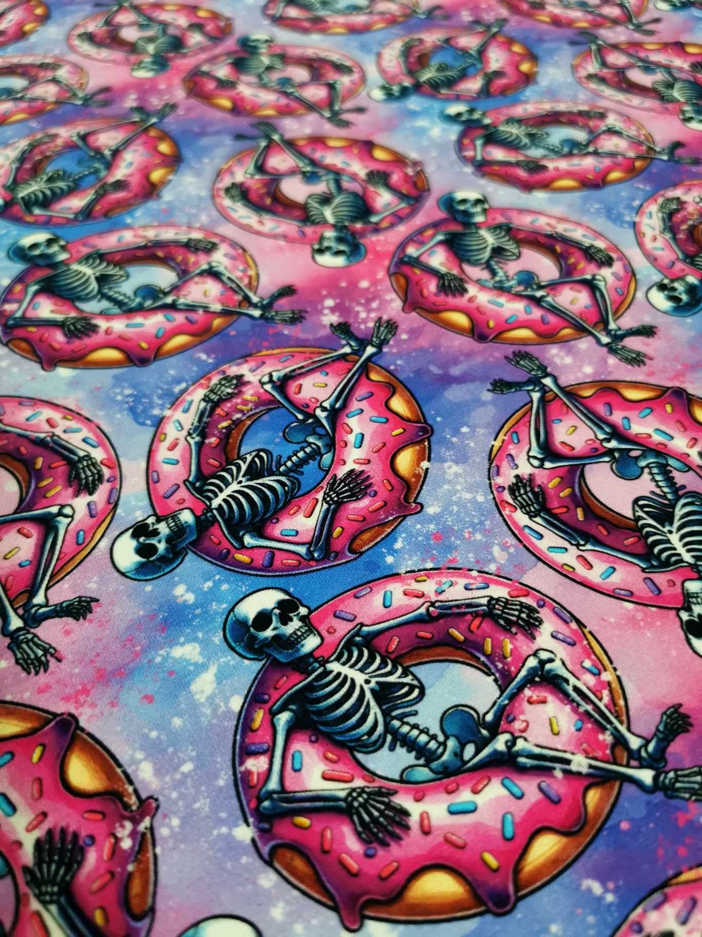 Fun pink skeletons in floating donuts on purple galaxy base, jersey fabric with 4 way stretch